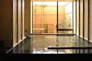 A hot spring bath with a wooden deck and a view of a bamboo garden outside. - Yadoya Tsubaki (Aomori)