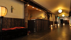 A hotel lobby with a reception desk, a wooden bench, and a wall-mounted lamp. - Yadoya Tsubaki (Aomori)