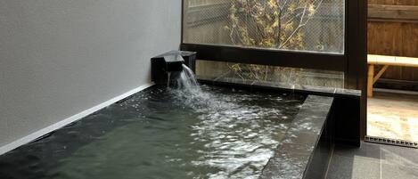 A hot spring bath area with a wooden bench and a view of a tree outside.