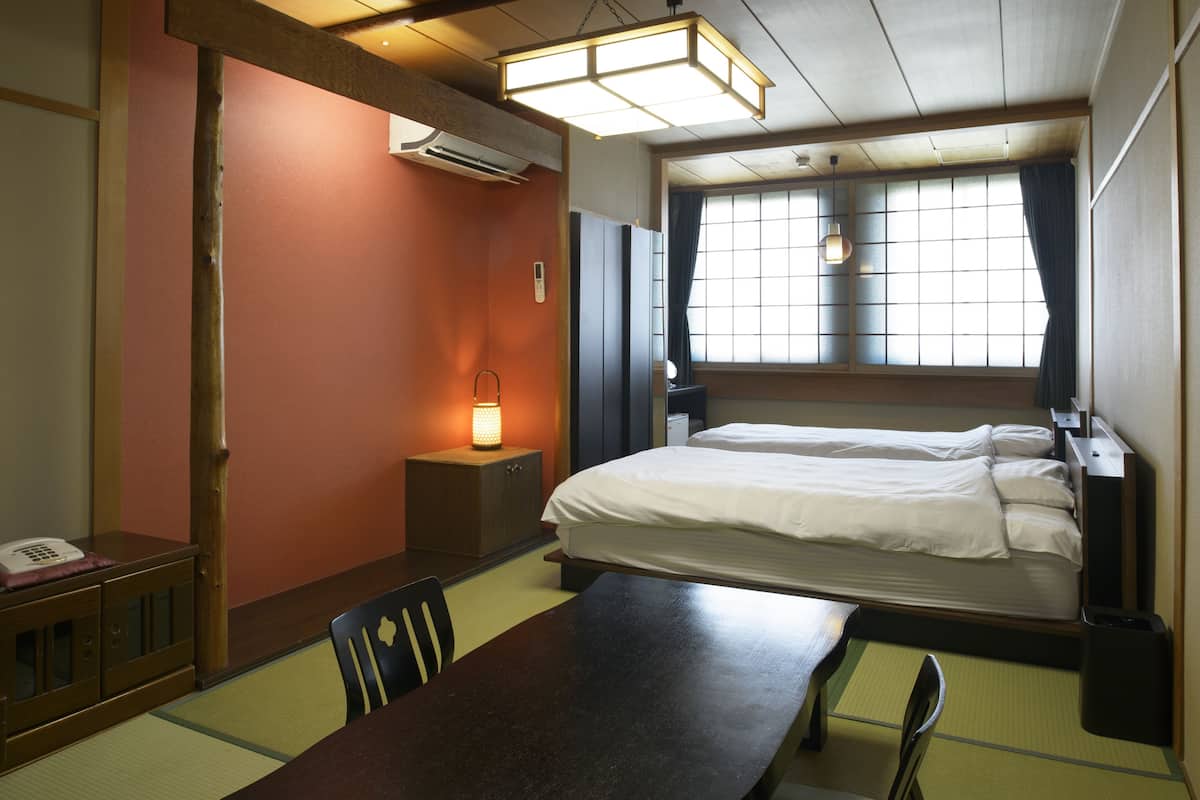 Une chambre d’hôtel équipée d’un lit, d’un bureau, d’une chaise, d’une table, d’une lampe et d’une fenêtre avec des rideaux.