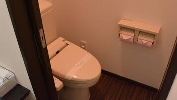 A small, compact bathroom with a toilet, a wall-mounted tissue dispenser, and a wooden floor.