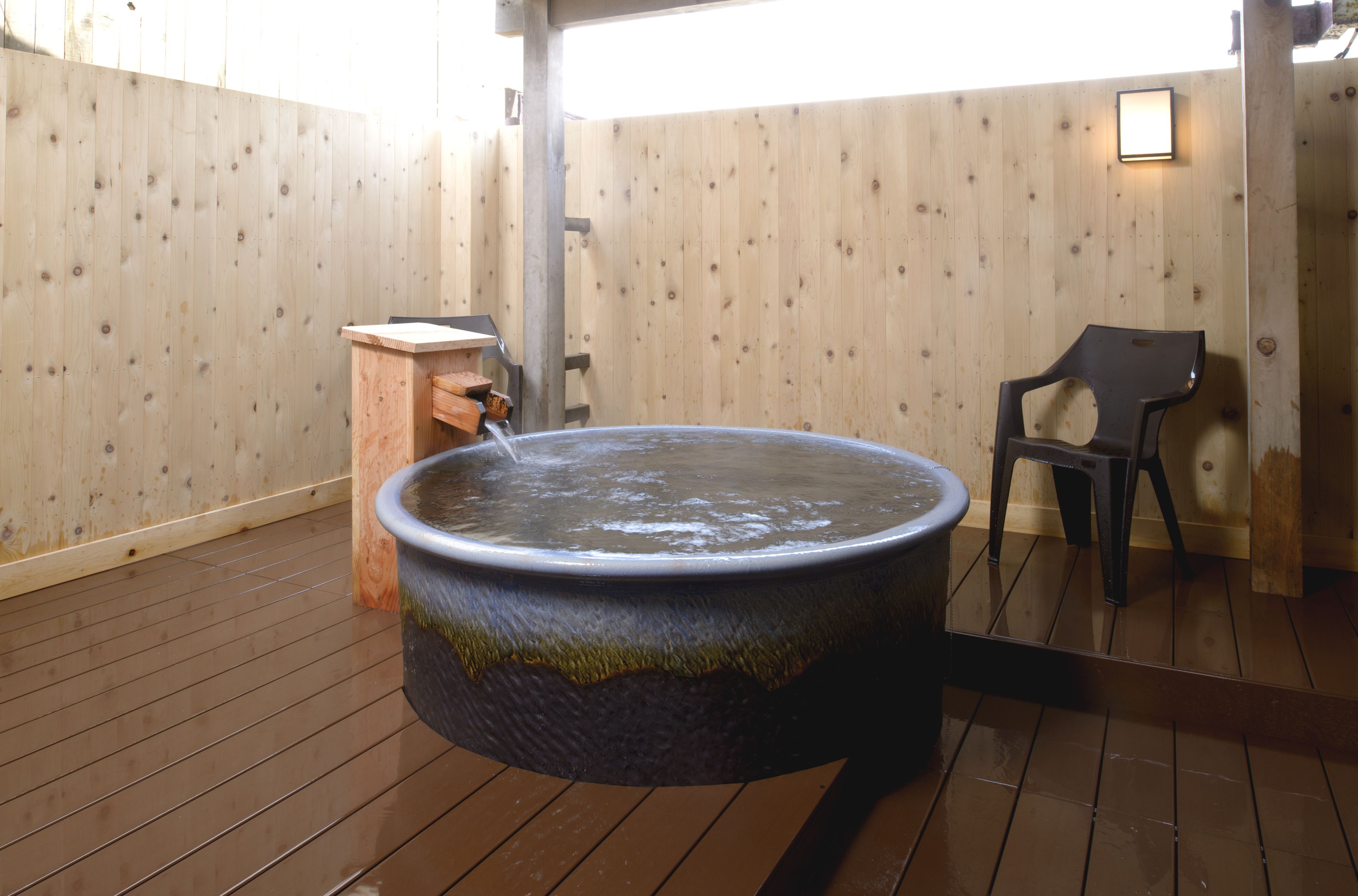 Zona d'una piscina interior amb sòl de fusta, que inclou una banyera d'hidromassatge, una banca de fusta i una taula petita de fusta.