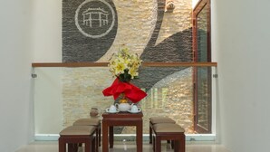 A modern interior with a glass railing, a stone wall with a circular design, and a table with a vase of flowers and white teacups. - Lantern Villa (Da Nang)