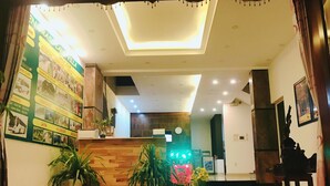 A hotel lobby with a wooden reception desk, potted plants, a wall with travel posters, and a modern ceiling design. - Lantern Villa (Da Nang)