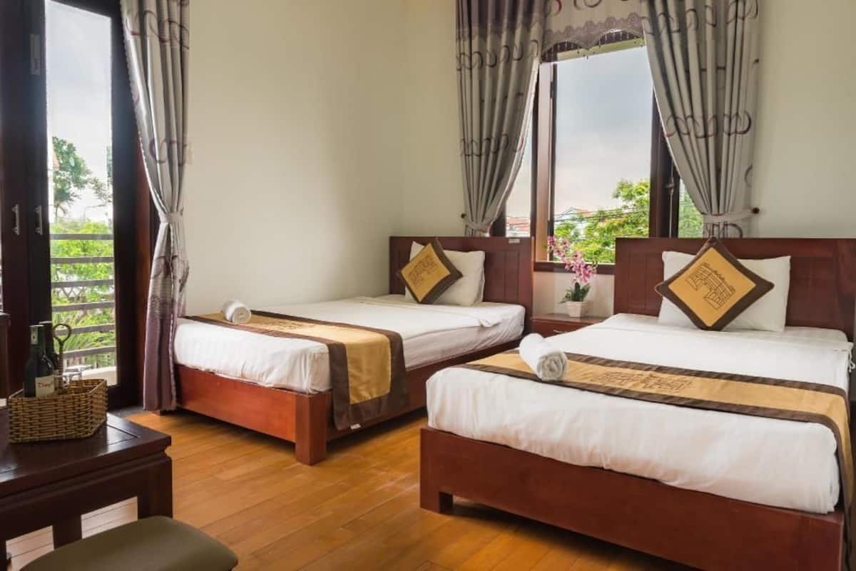 A hotel room with two wooden beds, a wooden nightstand, a wicker basket, and a view of greenery outside.
