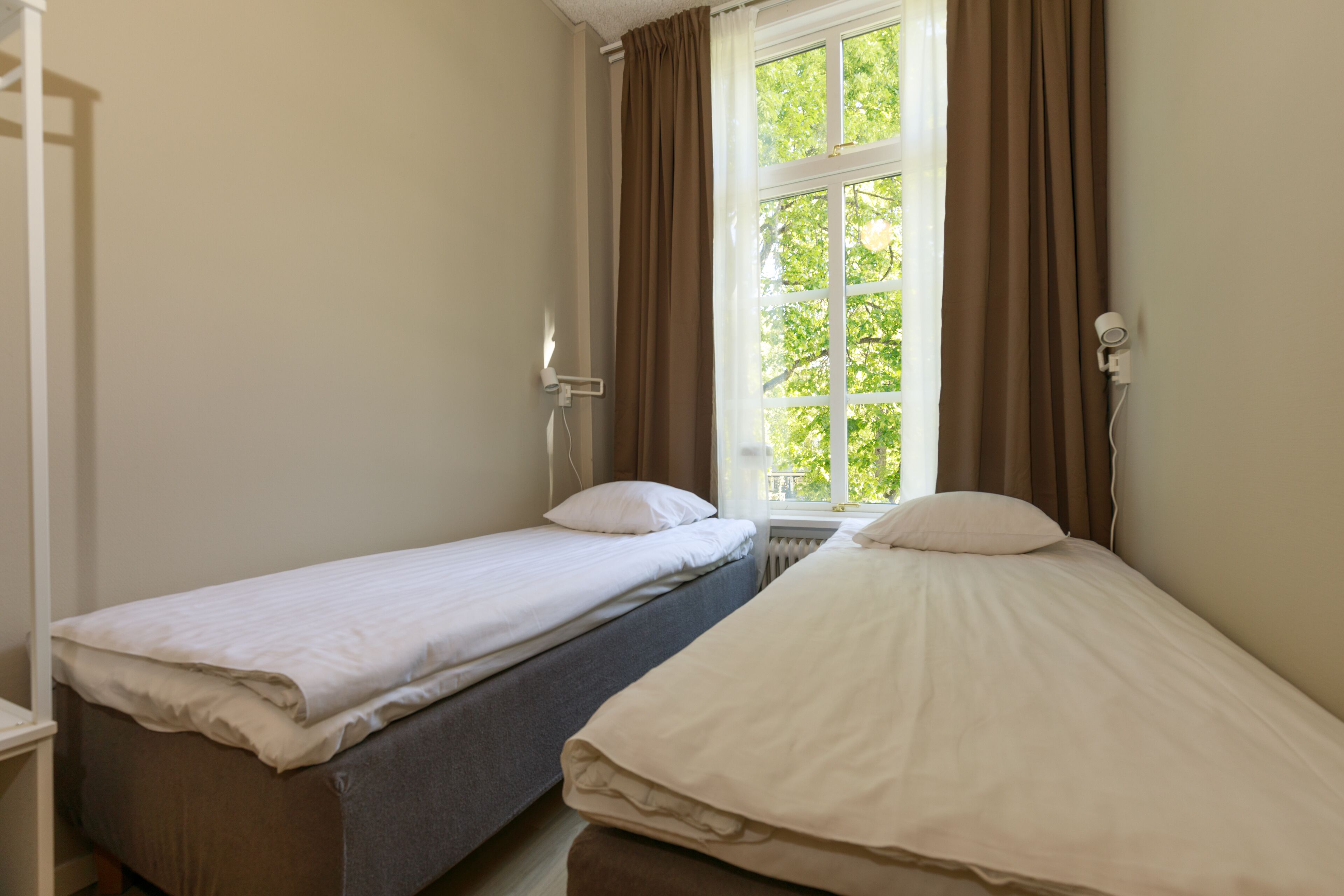 A room with two single beds, a window with curtains, and a radiator.