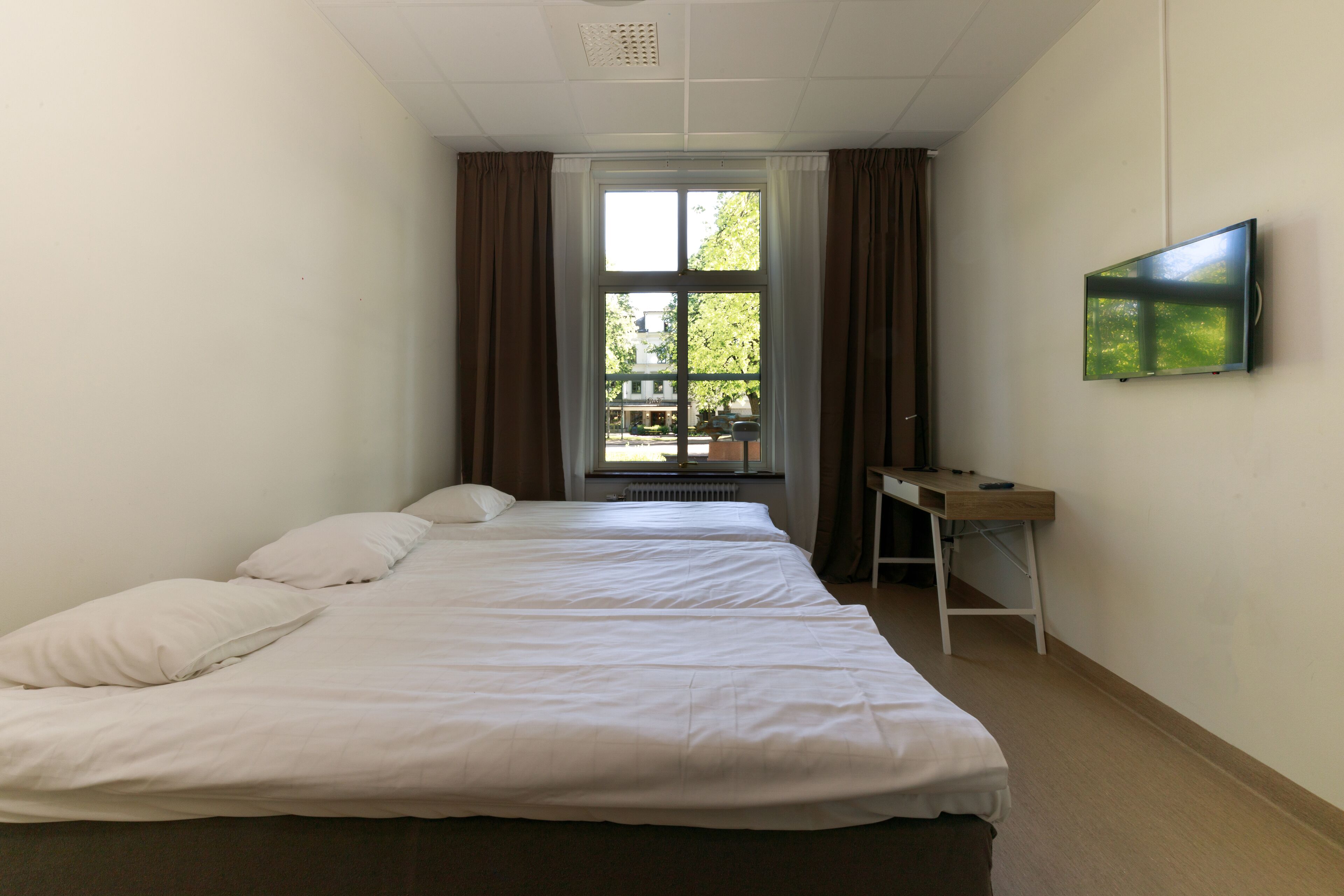 Ett hotellrum med två sängar, ett skrivbord och en tv på väggen.