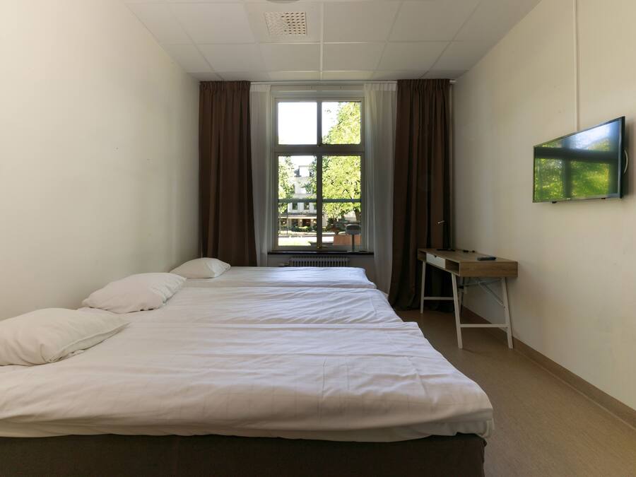 Ett hotellrum med två sängar, ett skrivbord och en tv på väggen.