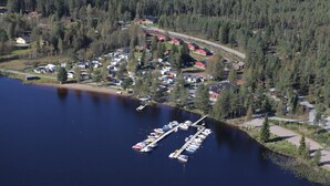 Luftaufnahme einer Siedlung am Seeufer mit einem Hafen, Häusern und dichtem Wald.