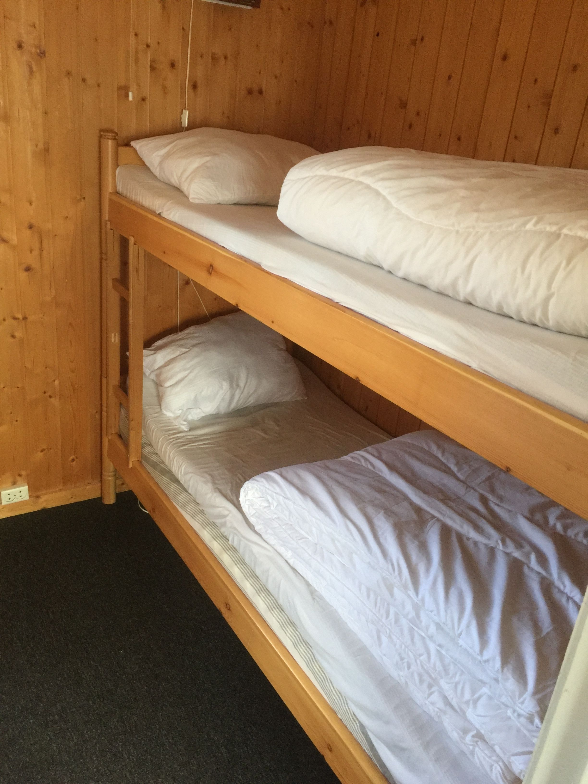 A bunk bed with white bedding in a wooden room.