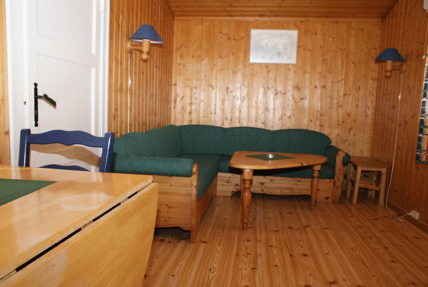 Um quarto acolhedor com paredes e chão de madeira, um sofá verde, uma mesa de madeira e duas luminárias.