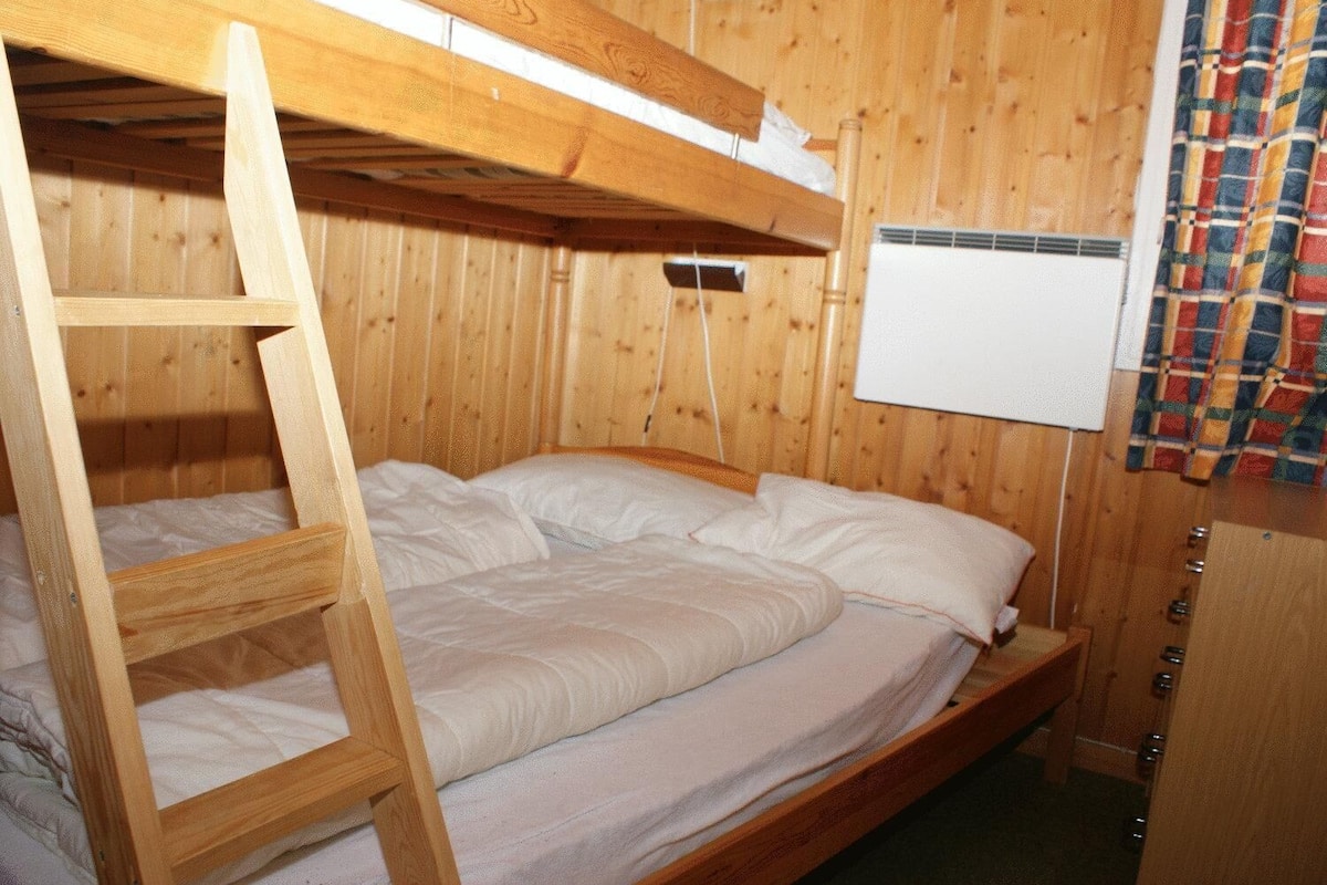 Ein hölzernes Etagenbett mit einer Leiter, weißer Bettwäsche und einer weißen Klimaanlage an der Wand.