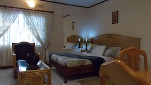 Ein Schlafzimmer mit einem Bett, einem Nachttisch aus Holz, einem Sessel, einem Tisch und einem Fenster mit Vorhängen.