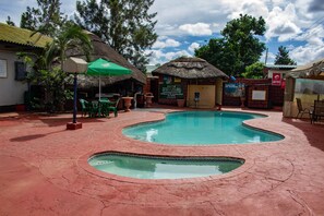 Une piscine bordée de briques, entourée d’un espace de détente extérieur et d’une structure à toit de chaume.