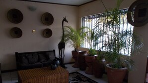 Ein Wohnzimmer mit einer Couch, einem Couchtisch, einer Giraffenskulptur, mehreren Blumentöpfen und einem gemusterten Teppich.