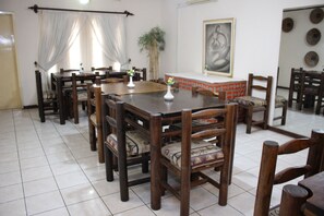 Un espace repas avec des tables et des chaises en bois, un grand tableau au mur et une plante.