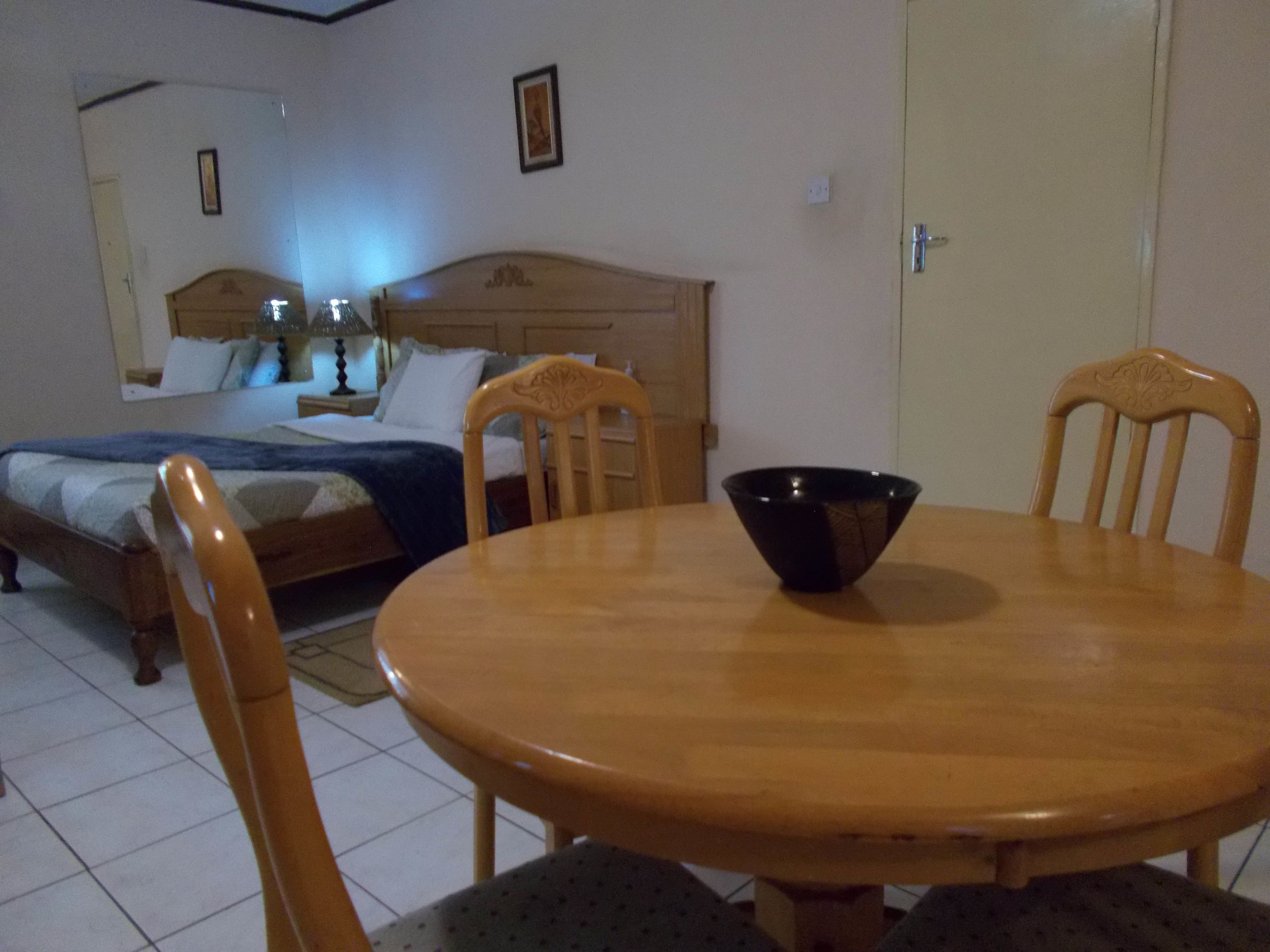 A bedroom with a bed, bedside table, lamp, and a dining table with chairs.