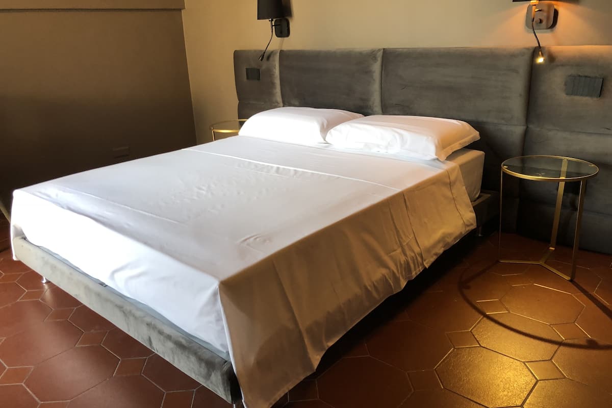 A neatly made bed with white linens, a grey headboard, and two bedside tables with lamps.