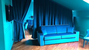 Quarto com sofá azul, TV fixada na parede e janela com cortinas.