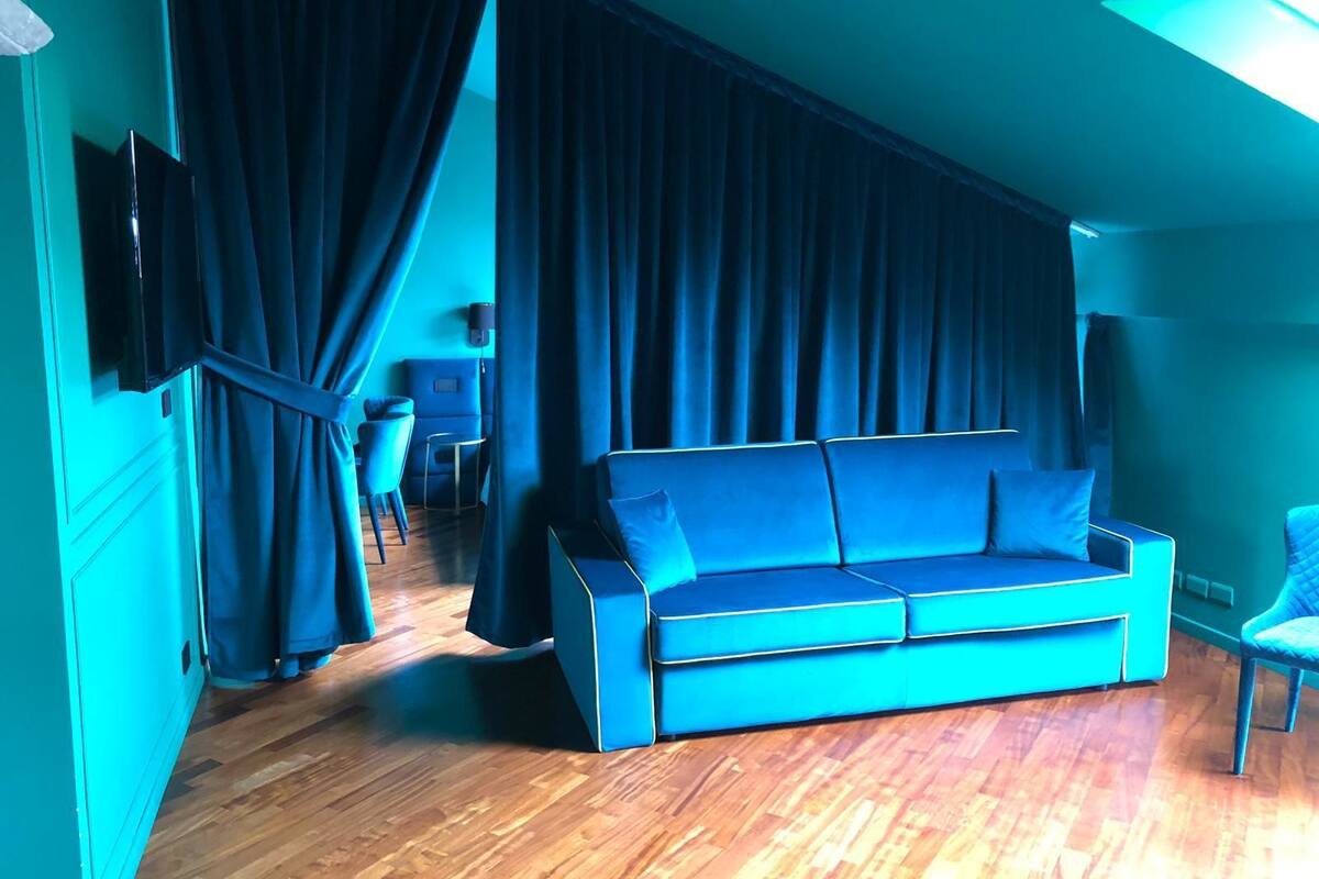 A room with a blue sofa, a TV mounted on the wall, and a window with curtains.
