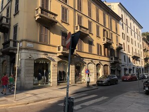 Una vista di strada con un edificio che mostra negozi di abbigliamento, un divieto di sosta e auto parcheggiate.