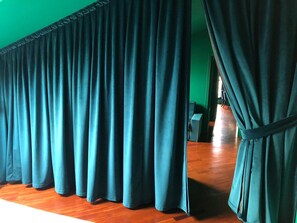 A room with a green wall and wooden flooring, featuring a set of teal curtains. - Garibaldi Suites (Milan)
