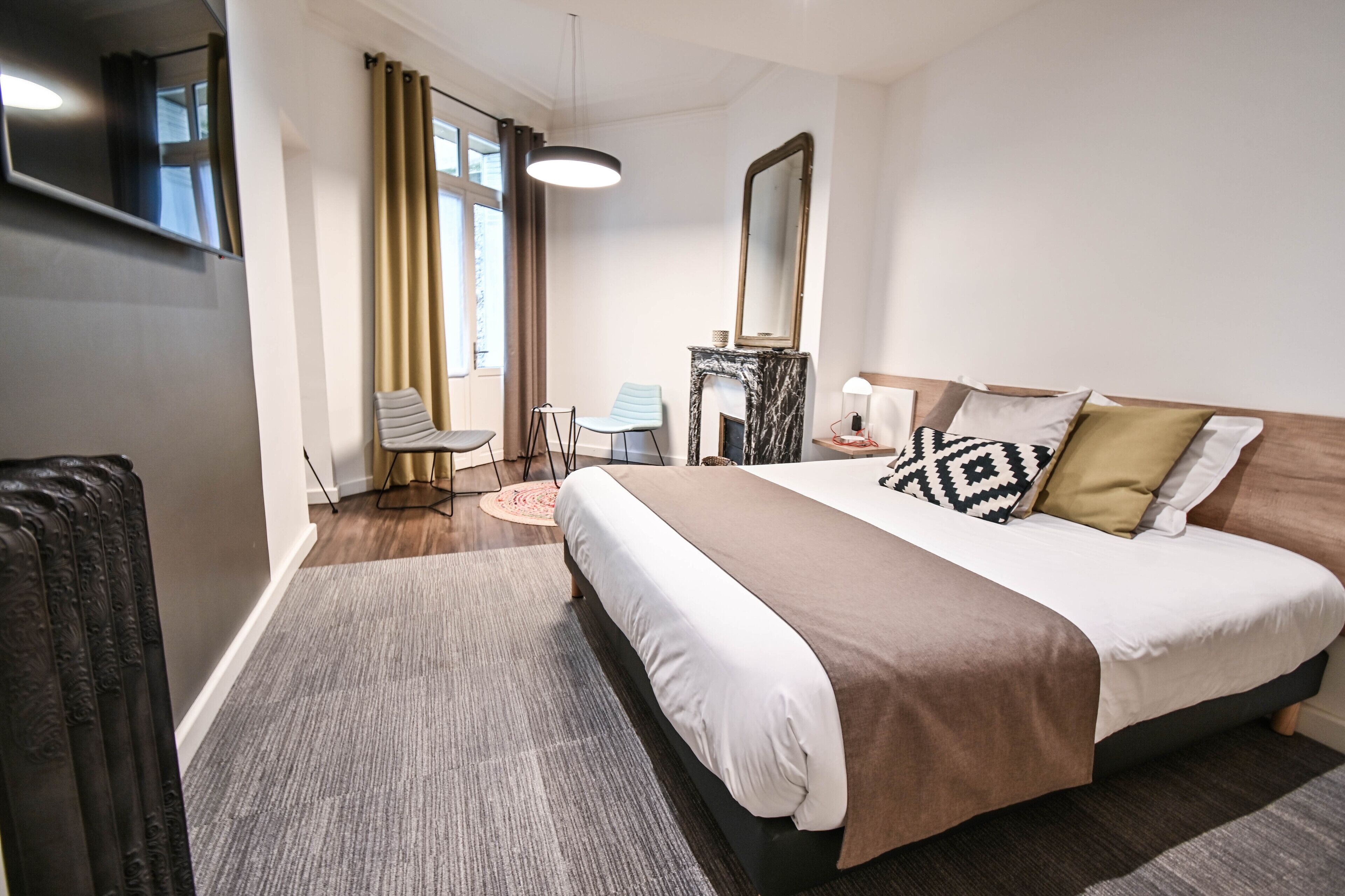 A modern hotel room with a large bed, a fireplace, a desk, and a chair.
