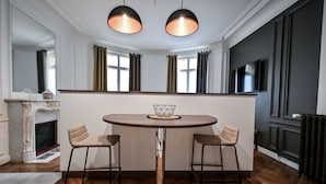 Un comedor moderno con una mesa redonda, dos taburetes de bar, lámparas colgantes, una chimenea y un televisor.