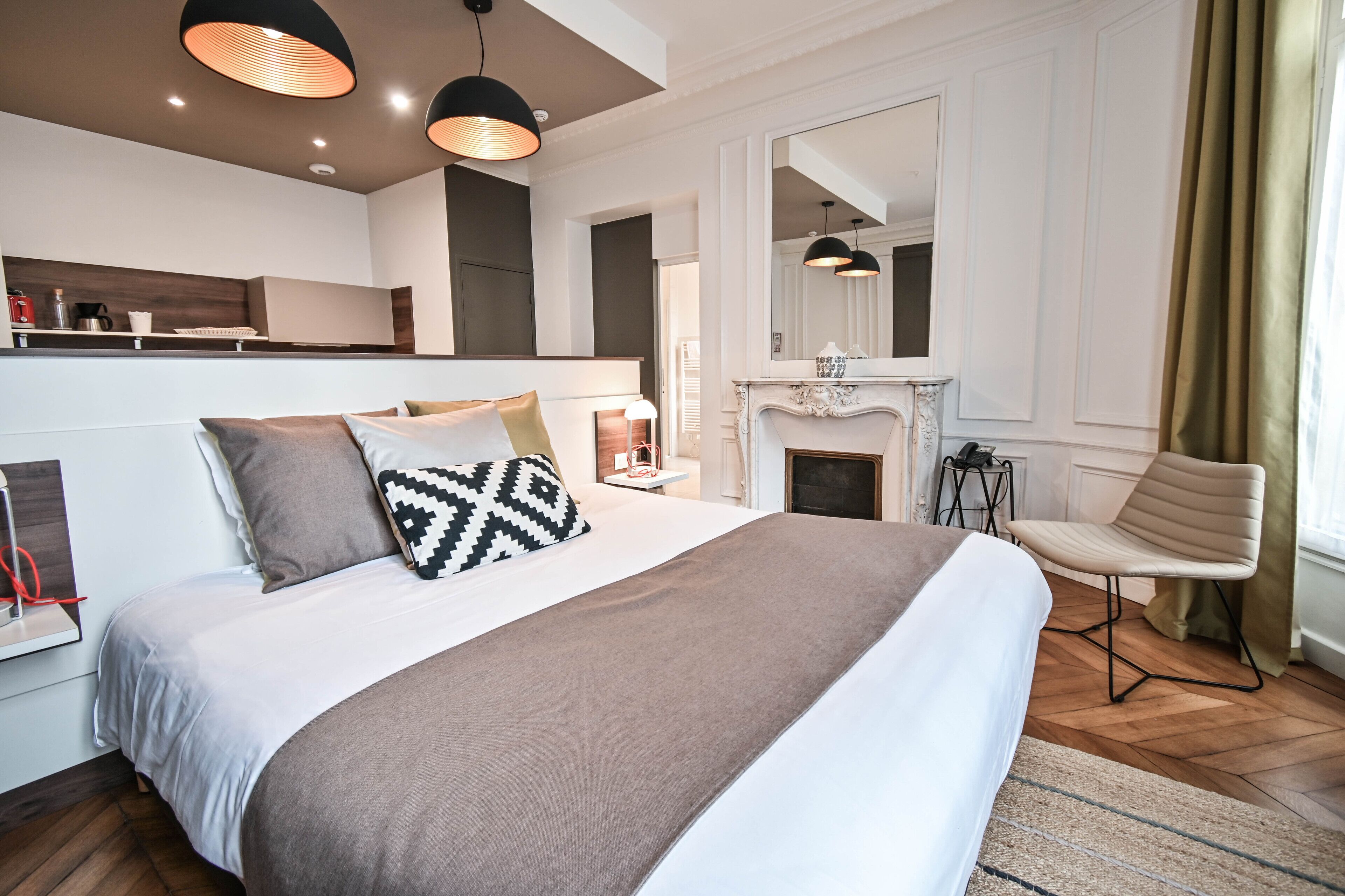A modern hotel room with a large bed, a fireplace, a dining area, and a view of the city.