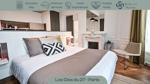 Habitación de hotel con cama, sillón, chimenea y vistas a la ciudad.