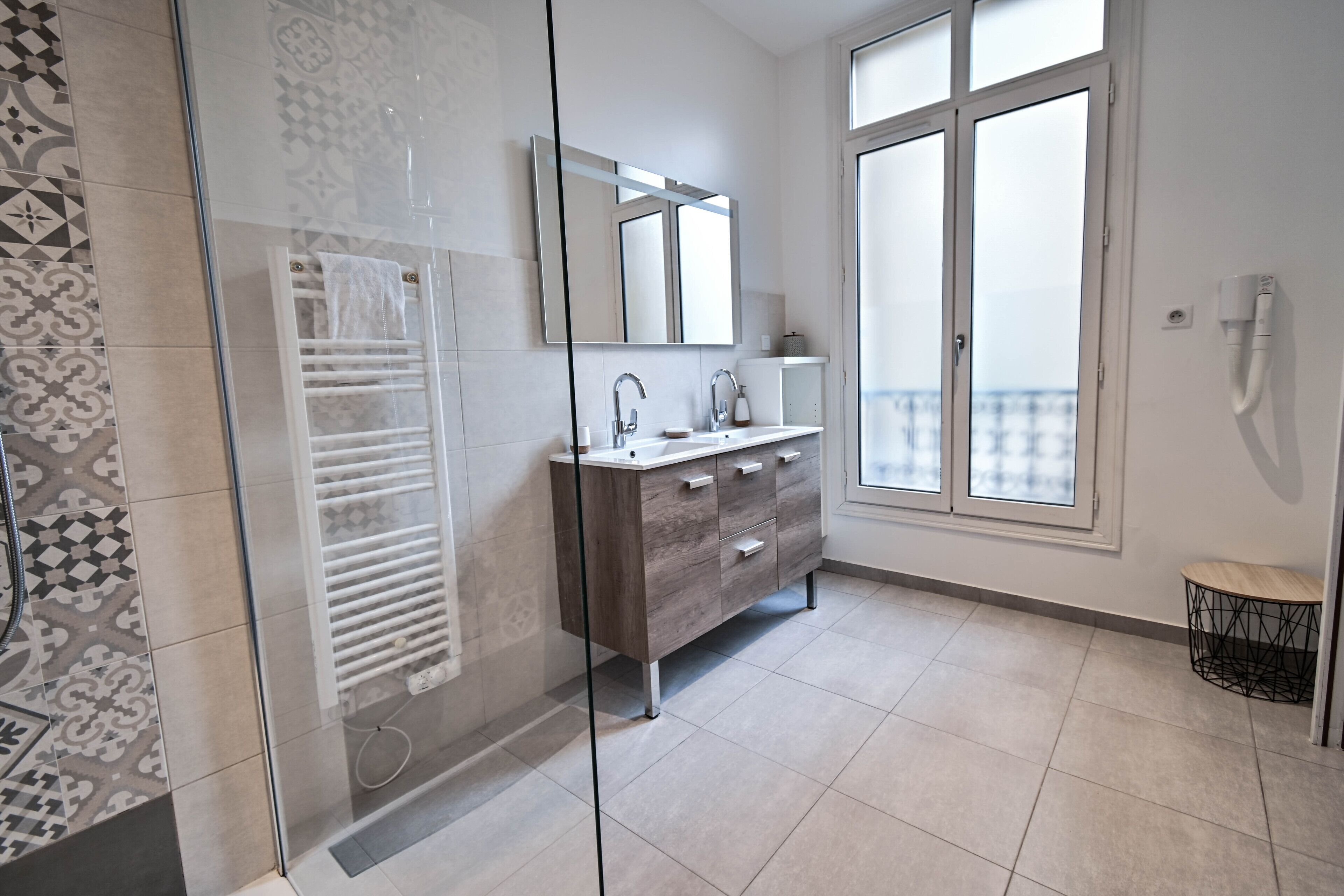 A modern bathroom with a glass shower enclosure, a vanity with a mirror, and a large window offering a view.