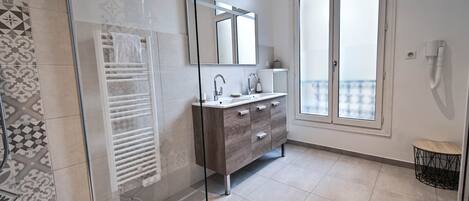 A modern bathroom with a glass shower enclosure, a vanity with a mirror, and a large window offering a view.