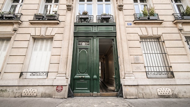 Fachada de edificio con puerta verde, varias ventanas y balcones con plantas.