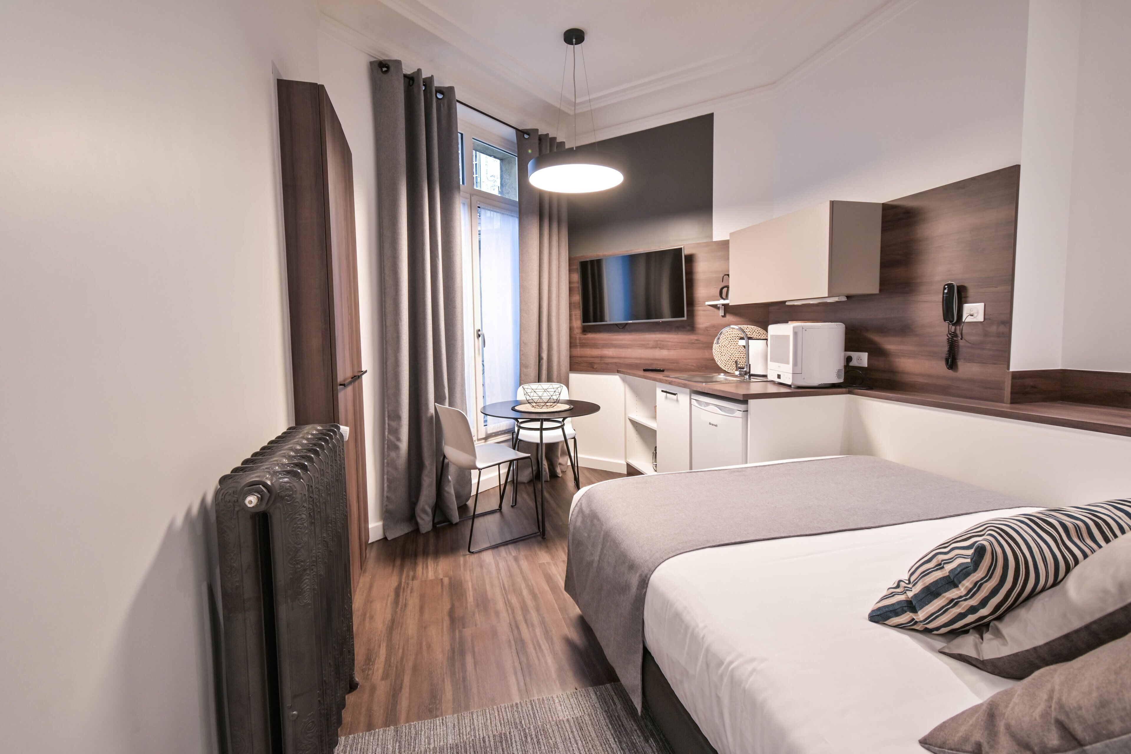 Een moderne hotelkamer met een bed, een bureau, een stoel en een kleine kitchenette.