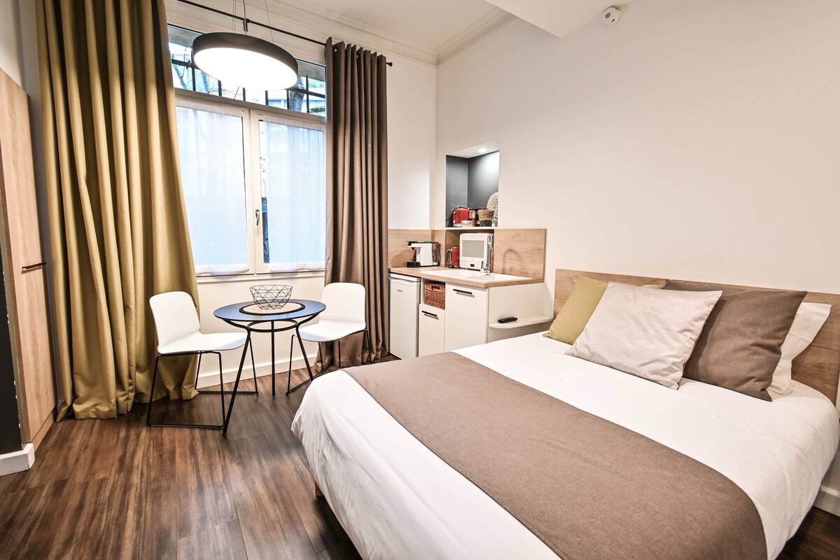 A hotel room with a bed, a desk, a chair, a microwave, and a window with curtains.