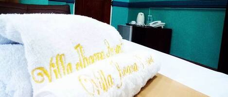 Un letto rifatto con cura, un asciugamano bianco con ricami dorati, una porta in legno e pareti color acquamarina.