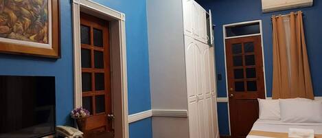 Habitación de hotel con cama, escritorio con televisor, armario y un cuadro en la pared.