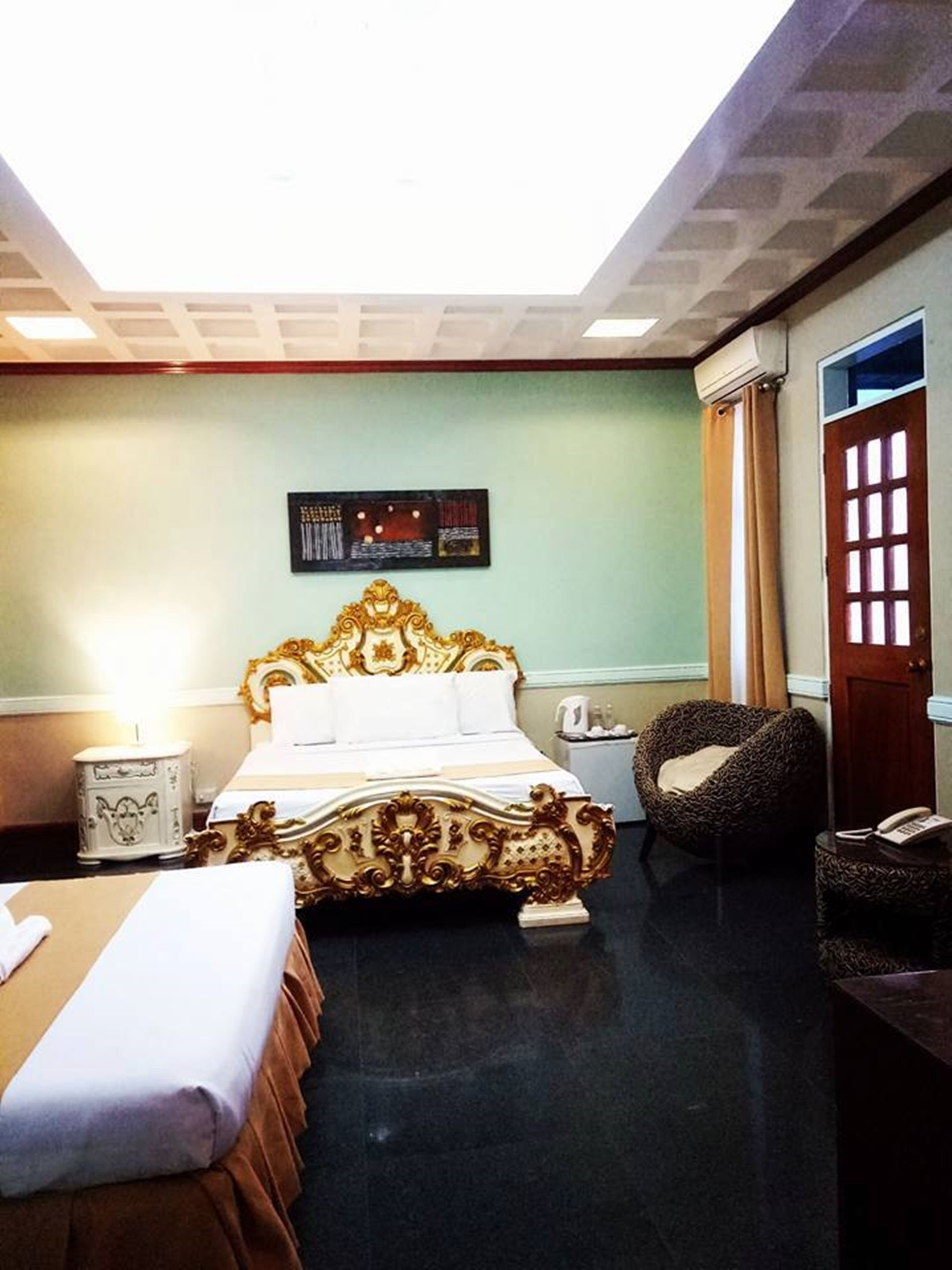 A hotel room with a large bed, a smaller bed, a chair, a nightstand, and a wall-mounted air conditioner.