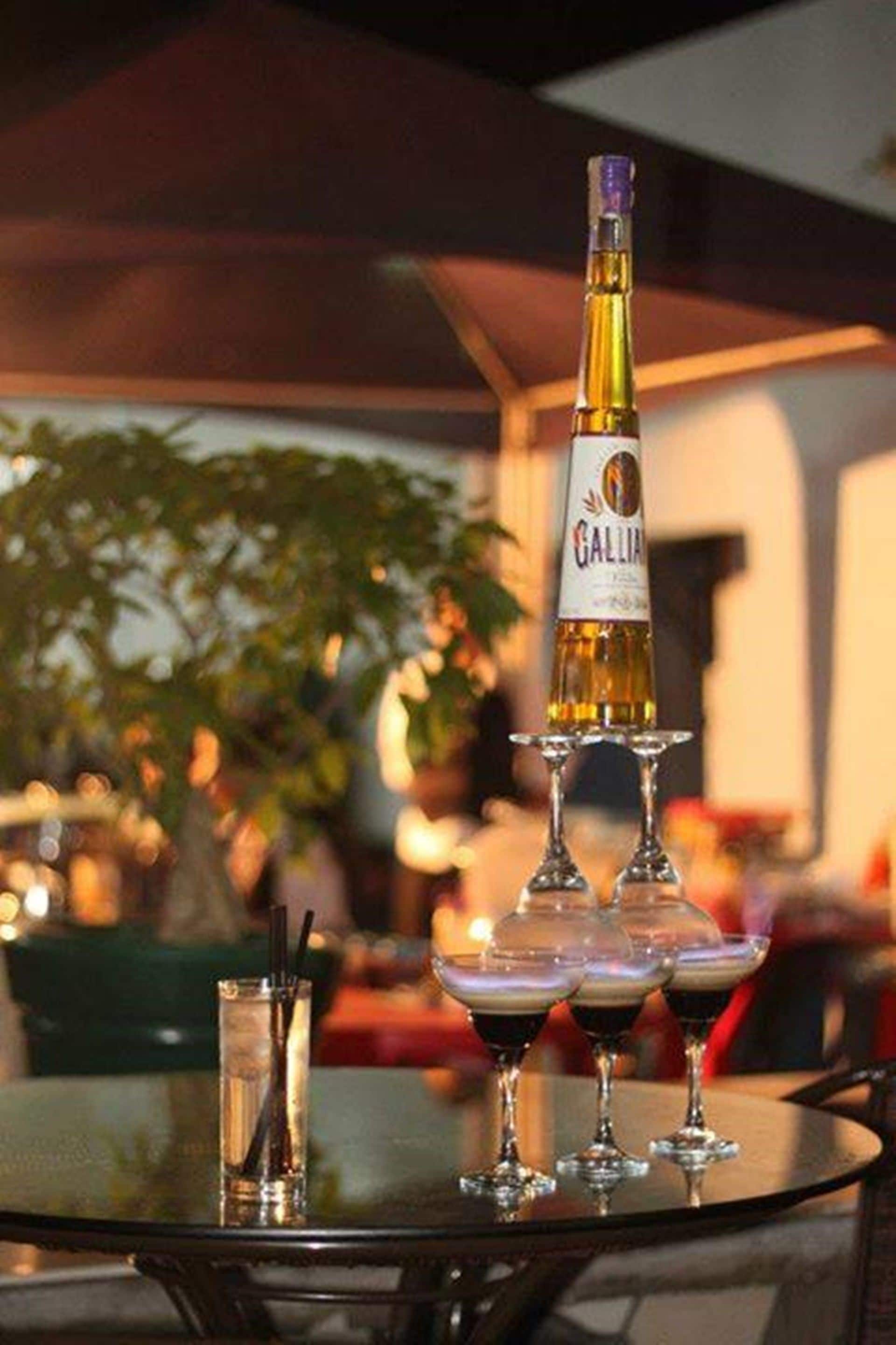 A bottle of Gallia wine on a table with four wine glasses, one of which is filled.