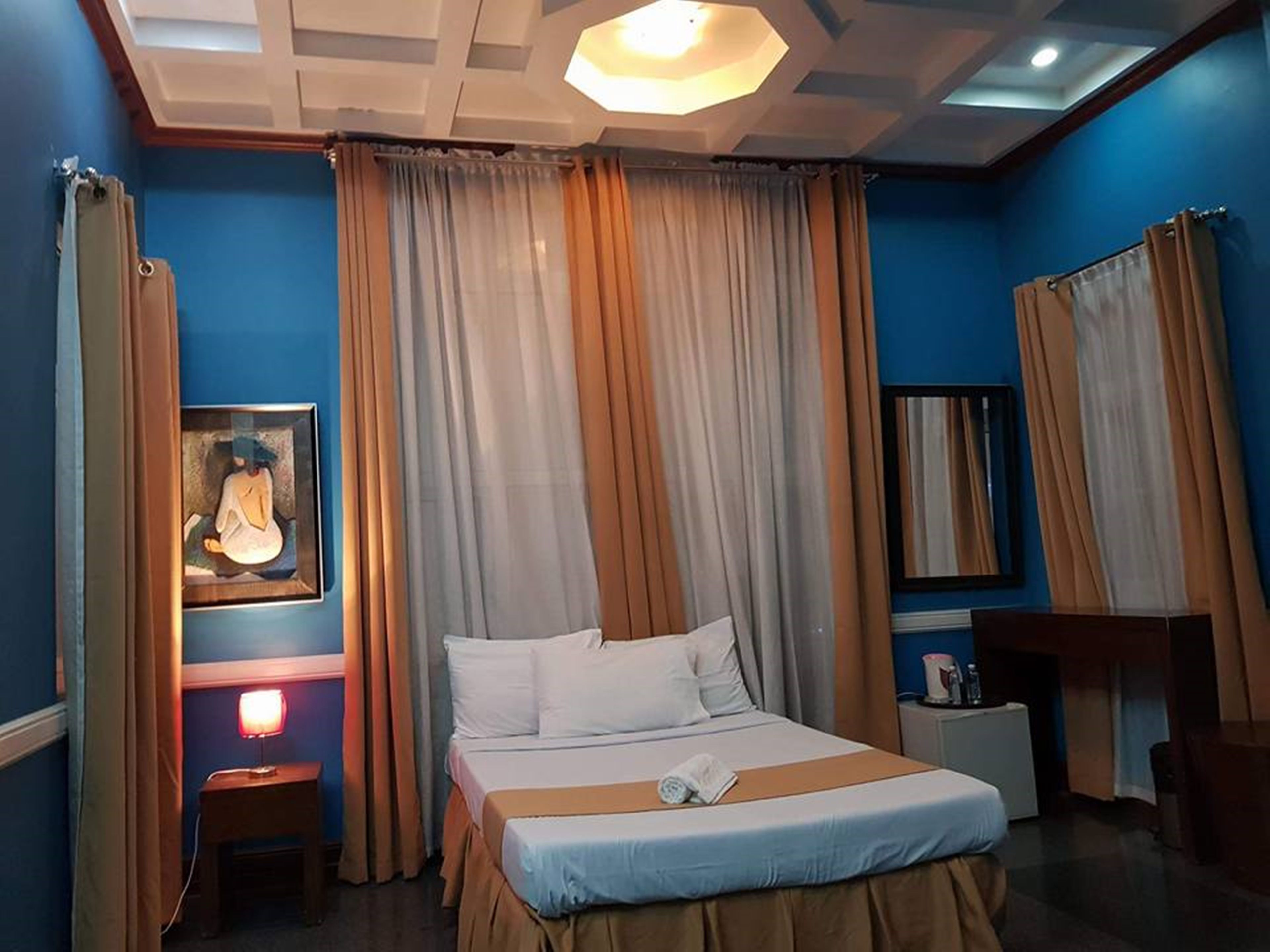 A hotel room with a bed, a nightstand, a lamp, a painting, and a mirror.