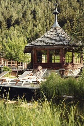 A wooden gazebo with a thatched roof, surrounded by lush greenery and a wooden deck with lounge chairs. - Residence Lusina (Luson)