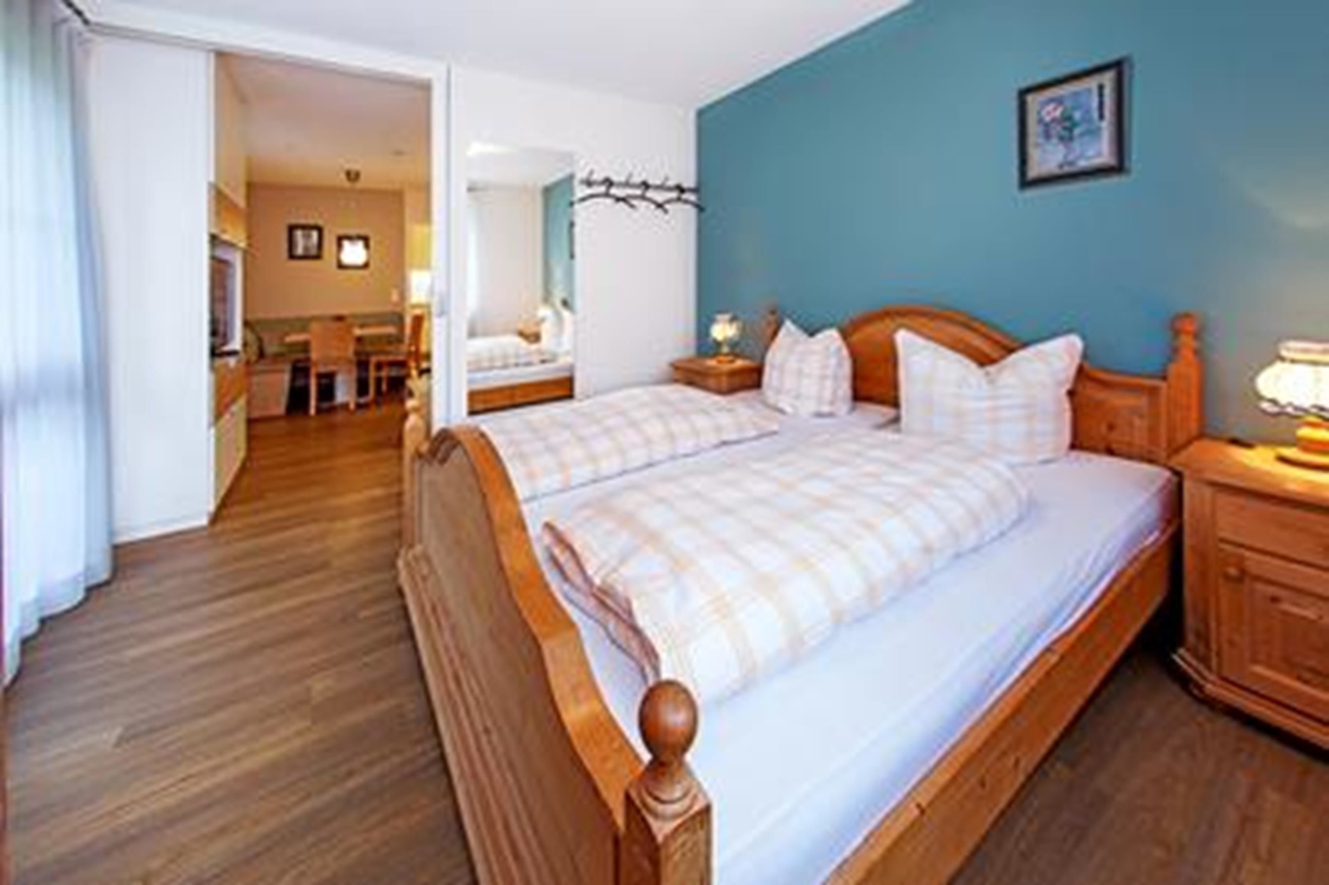 A bedroom with two beds, wooden headboards, a nightstand with a lamp, and a blue wall.