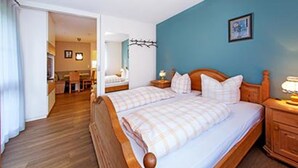 A bedroom with two beds, wooden headboards, a nightstand with a lamp, and a blue wall. - Ferienwohnung Sturm (Reit im Winkl)