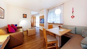 A cozy living room with a sofa, a dining table with chairs, and a TV in the background. - Ferienwohnung Sturm (Reit im Winkl)