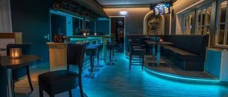 A bar area with blue lighting, a seating area with a sofa, and a counter with stools.