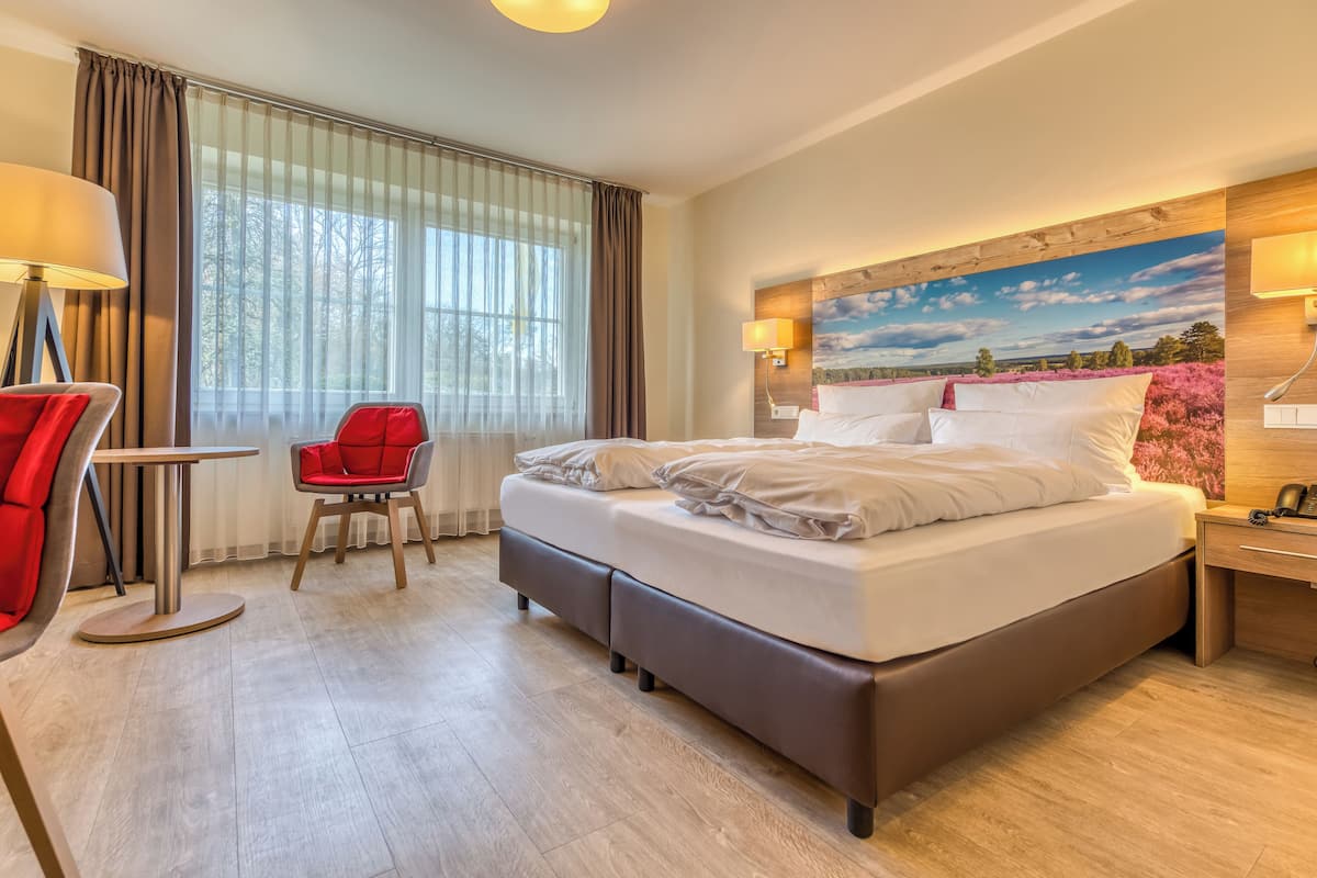 A hotel room with a large bed, a desk, a chair, and a window with curtains.