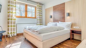 Quarto moderno com piso de madeira, cama com roupa de cama branca, janela com cortinas e mesa de cabeceira com abajur.