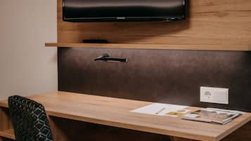 Et moderne kontor med et træskrivebord, en sort stol med mønster, et ophængt fladskærms-tv og en stikkontakt.