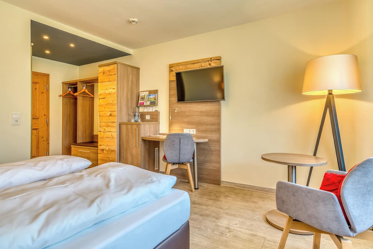 A hotel room with a bed, a desk, a chair, a TV mounted on the wall, and a lamp.