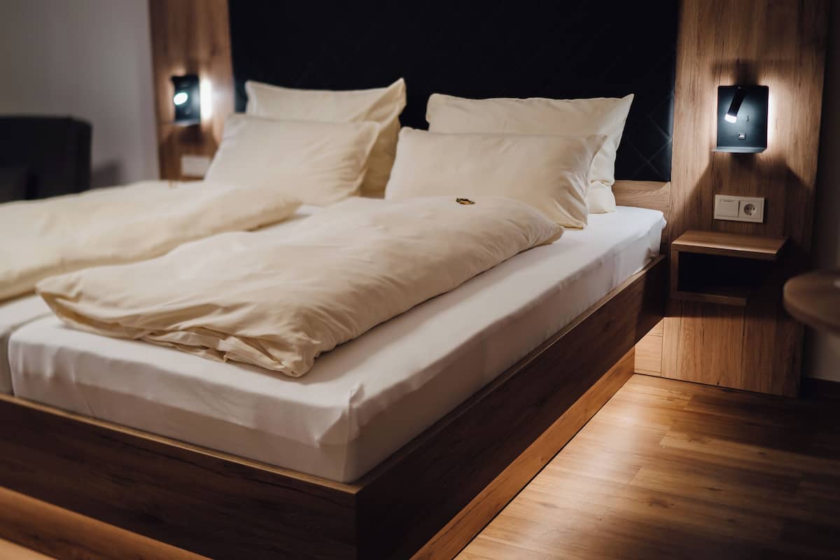 A neatly made bed with white linens and pillows, wooden headboard, and bedside tables with wall-mounted lamps.